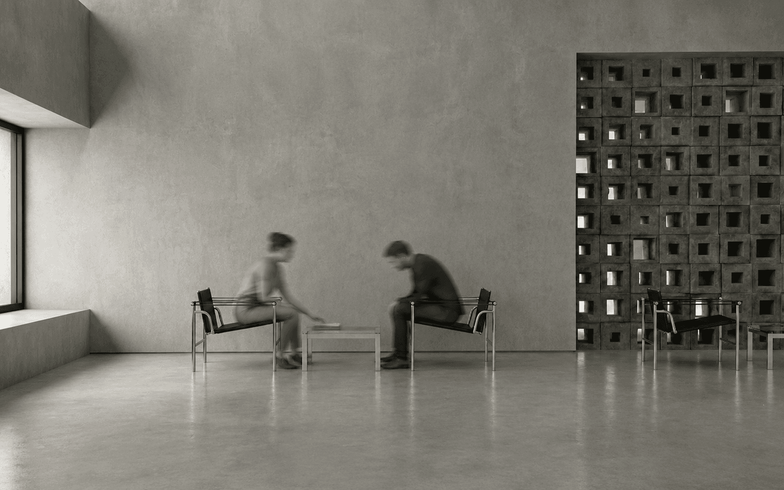 A pair of black leather lounge chairs at a low table beside the perforated stone block screen.