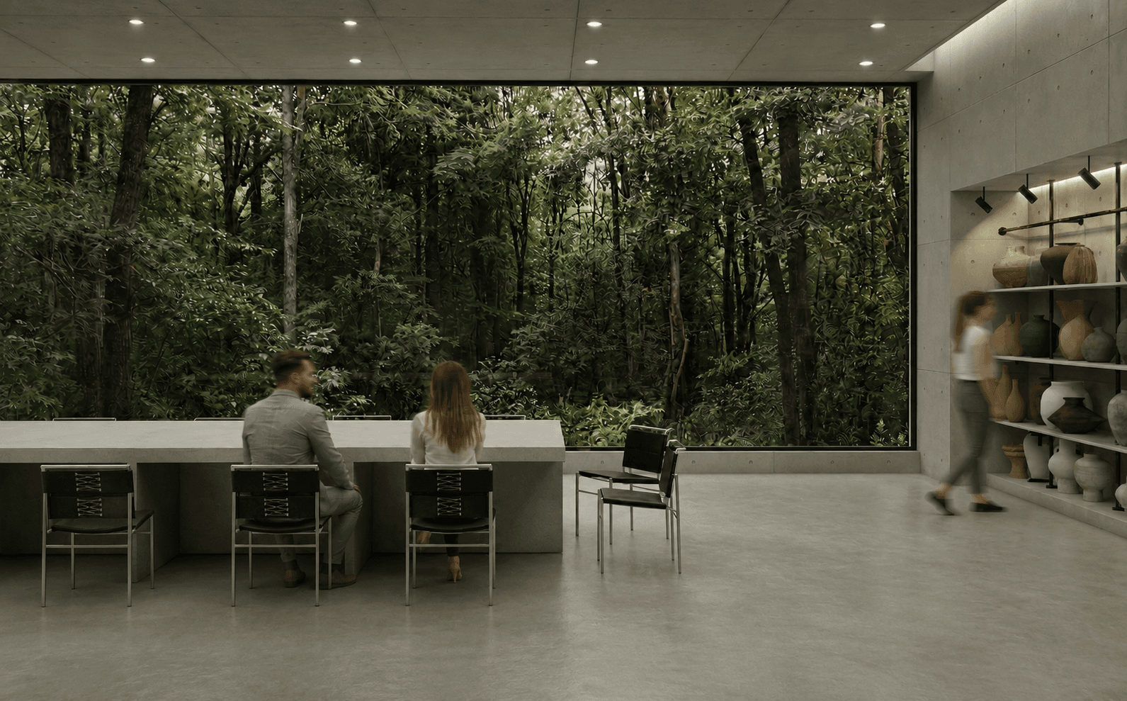 Workshop interior: a long concrete table facing a full-height window filled entirely with forest, people seated along it.
