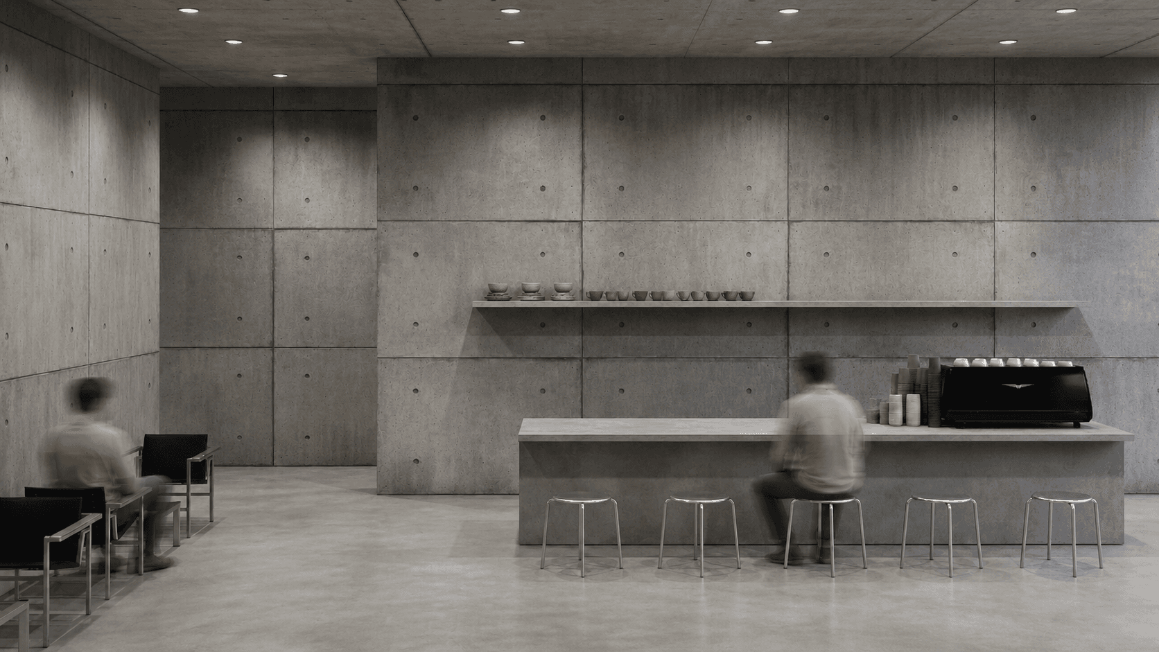 Workshop café: a concrete counter with cups and an espresso machine, people seated on steel stools and chairs.
