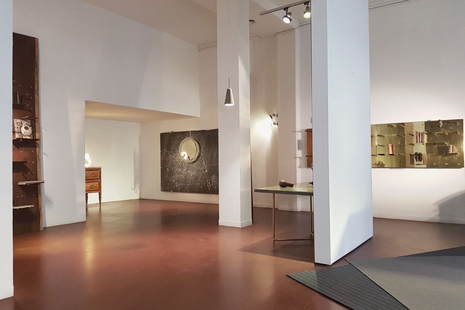 The existing Brera interior before the fit-out: white walls and columns over a terracotta floor, with freestanding gallery shelving and display pieces still in place.
