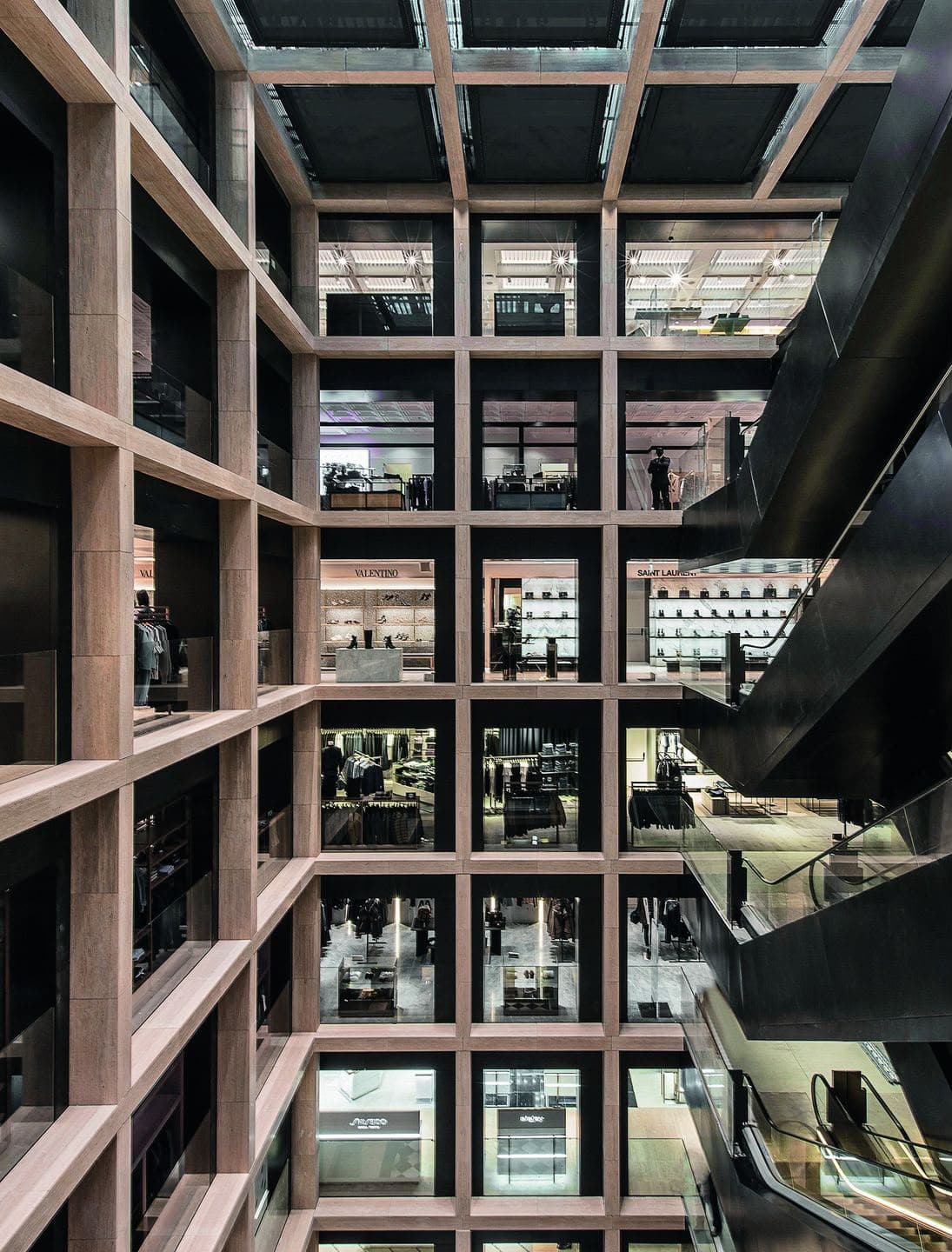 The Rinascente atrium seen from within: the travertine structural grid rising past several retail floors beside an escalator run.